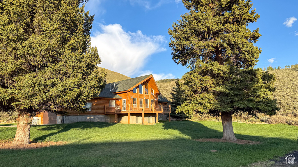 Back of house featuring a yard, a wooden deck, log exterior, and roof with shingles