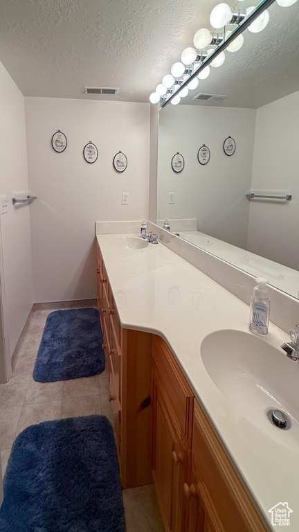Full bathroom with double vanity, a textured ceiling, and tile patterned flooring