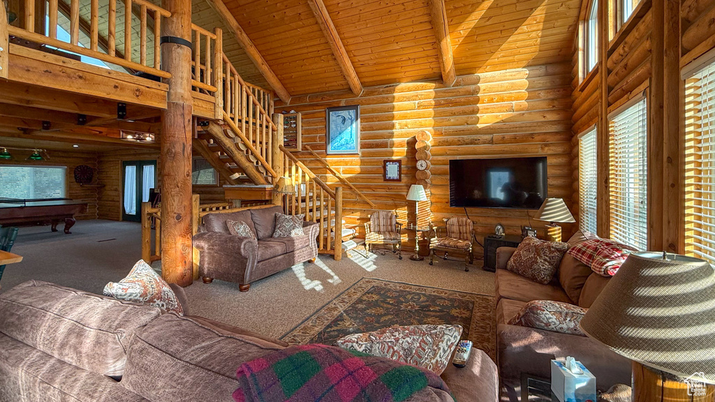 Carpeted living room featuring log walls, high vaulted ceiling, pool table, wooden ceiling with exposed beams, and stairs