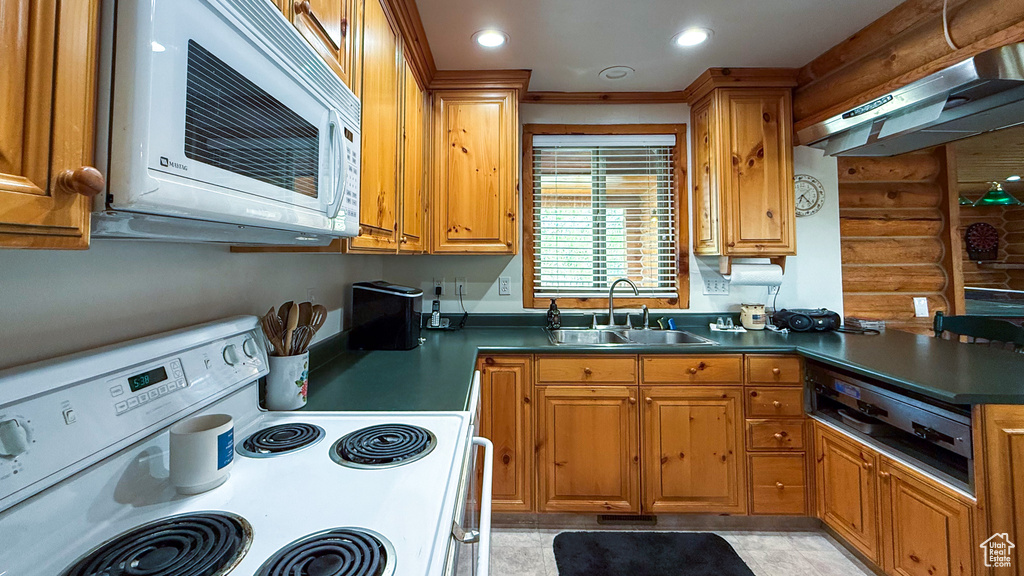 Kitchen with white electric range oven, a sink, rustic walls, under cabinet range hood, and dark countertops