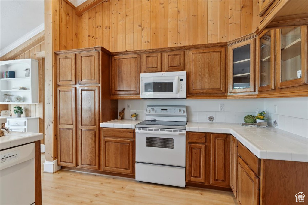 Kitchen featuring white appliances, brown cabinets, tile countertops, light wood finished floors, and wood walls