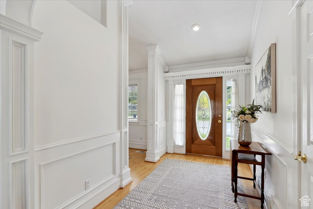 Foyer featuring ornamental molding, a decorative wall, light wood-style flooring, a wainscoted wall, and decorative columns