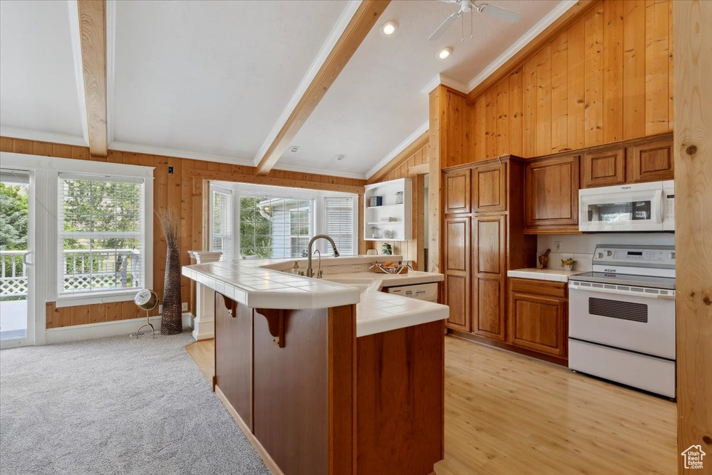 Kitchen with white appliances, tile countertops, wooden walls, a sink, and brown cabinetry