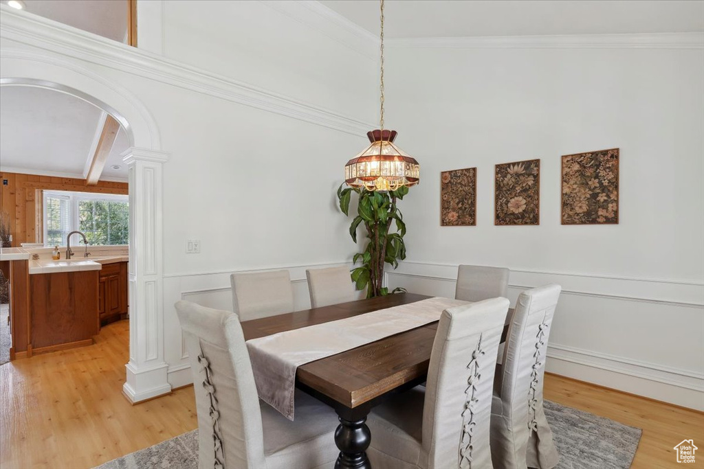 Dining room with arched walkways, light wood finished floors, a chandelier, a decorative wall, and a wainscoted wall
