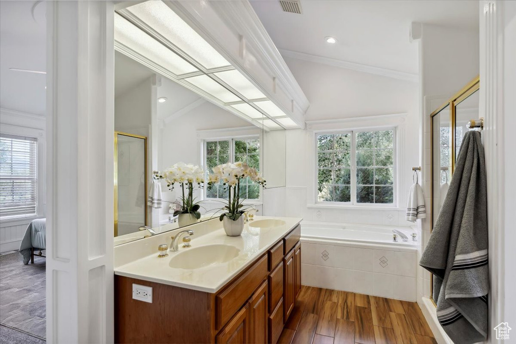 Full bathroom featuring a bath, double vanity, wood finished floors, crown molding, and a shower with door