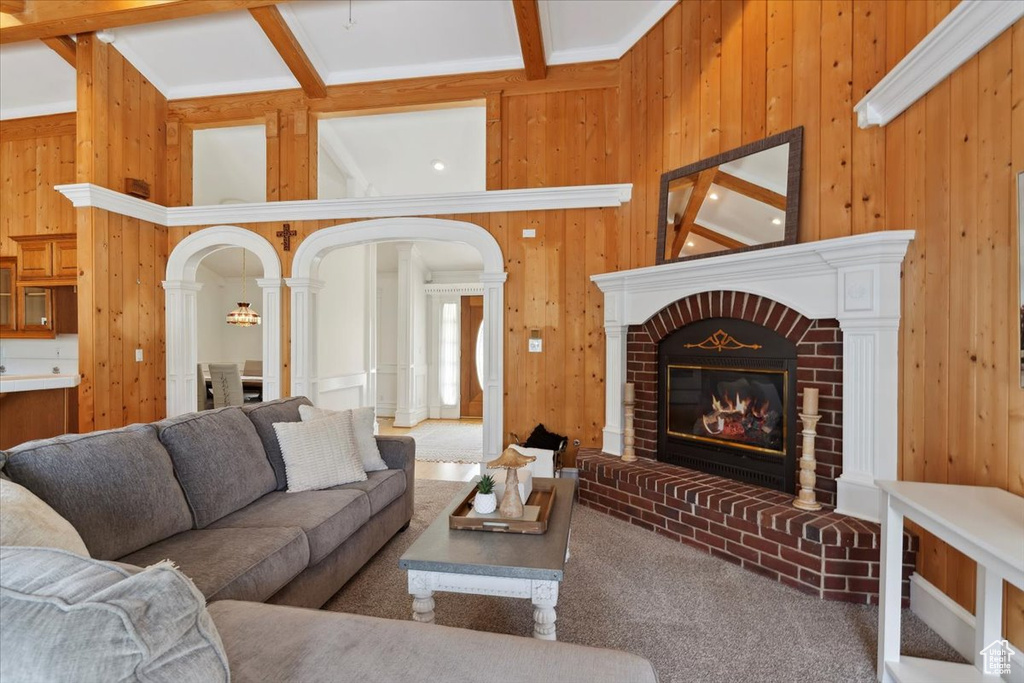 Carpeted living room with wooden walls, a fireplace, arched walkways, beam ceiling, and decorative columns