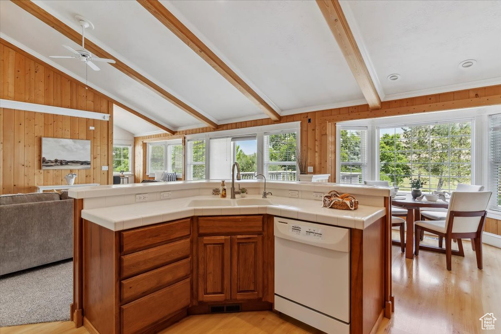Kitchen featuring white dishwasher, a sink, open floor plan, plenty of natural light, and wooden walls