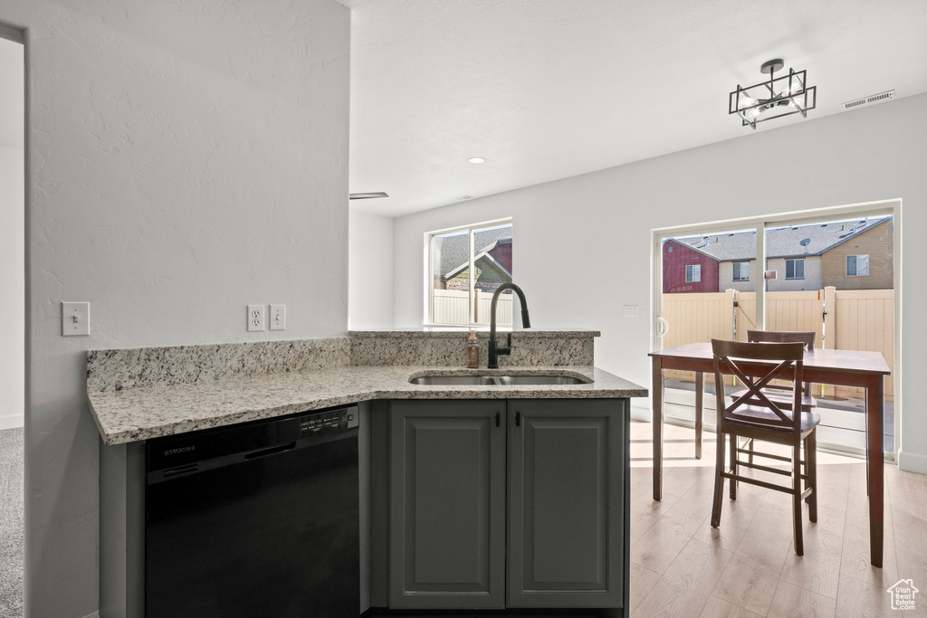 Kitchen with black dishwasher, a sink, light stone counters, light wood-type flooring, and gray cabinetry