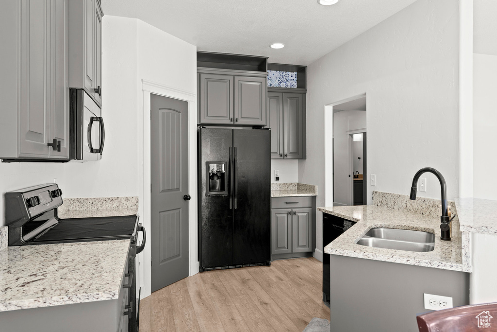 Kitchen featuring black fridge with ice dispenser, stainless steel electric range oven, gray cabinets, a sink, and light wood-style floors