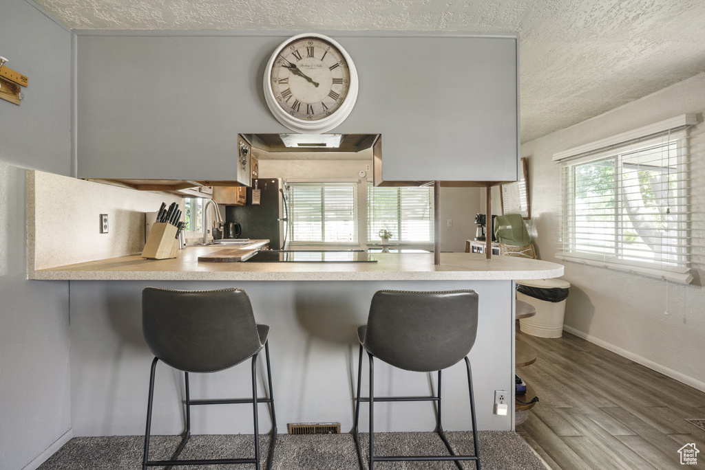 Kitchen with a textured ceiling, wood finished floors, plenty of natural light, and a breakfast bar