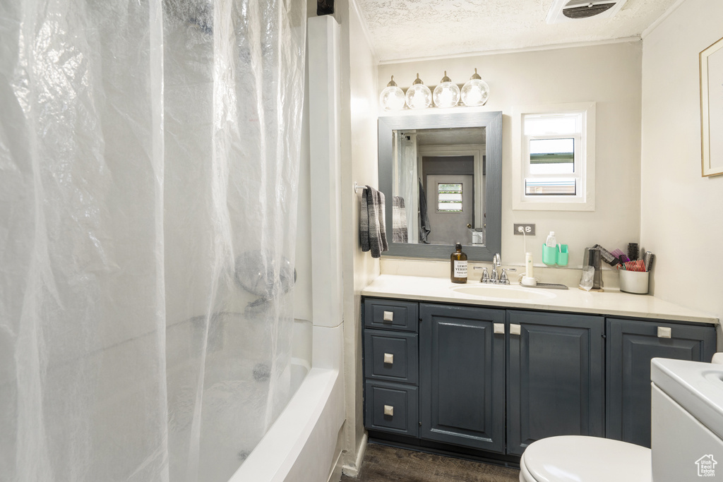 Bathroom featuring vanity, toilet, shower / tub combo with curtain, a textured ceiling, and wood finished floors