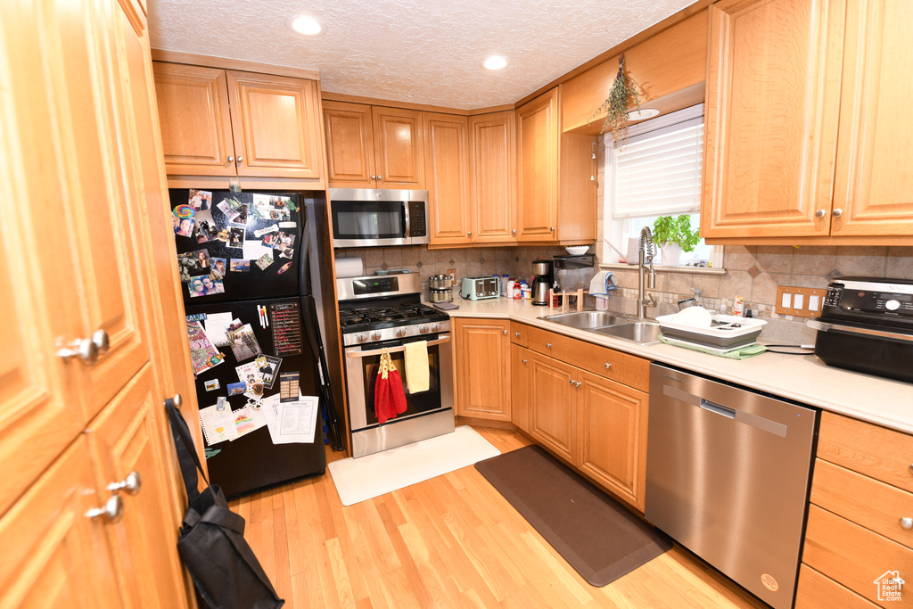 Kitchen with stainless steel appliances, light countertops, light wood-type flooring, tasteful backsplash, and a textured ceiling