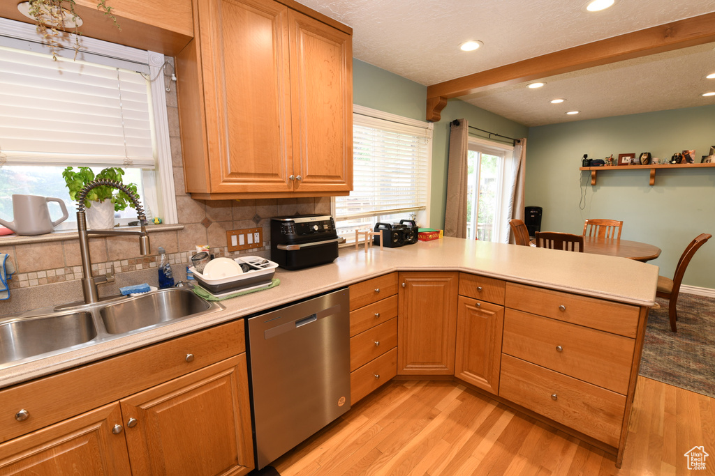 Kitchen with dishwasher, a peninsula, light wood-style flooring, tasteful backsplash, and light countertops