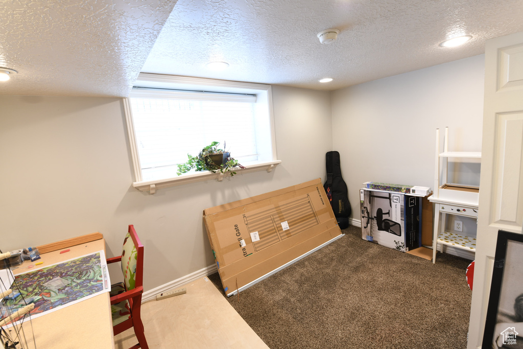Office area with a textured ceiling, dark carpet, and baseboards