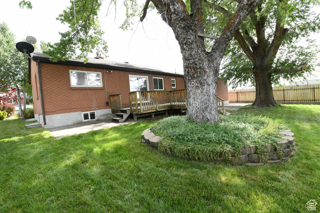 Back of house featuring a wooden deck, a patio, and brick siding