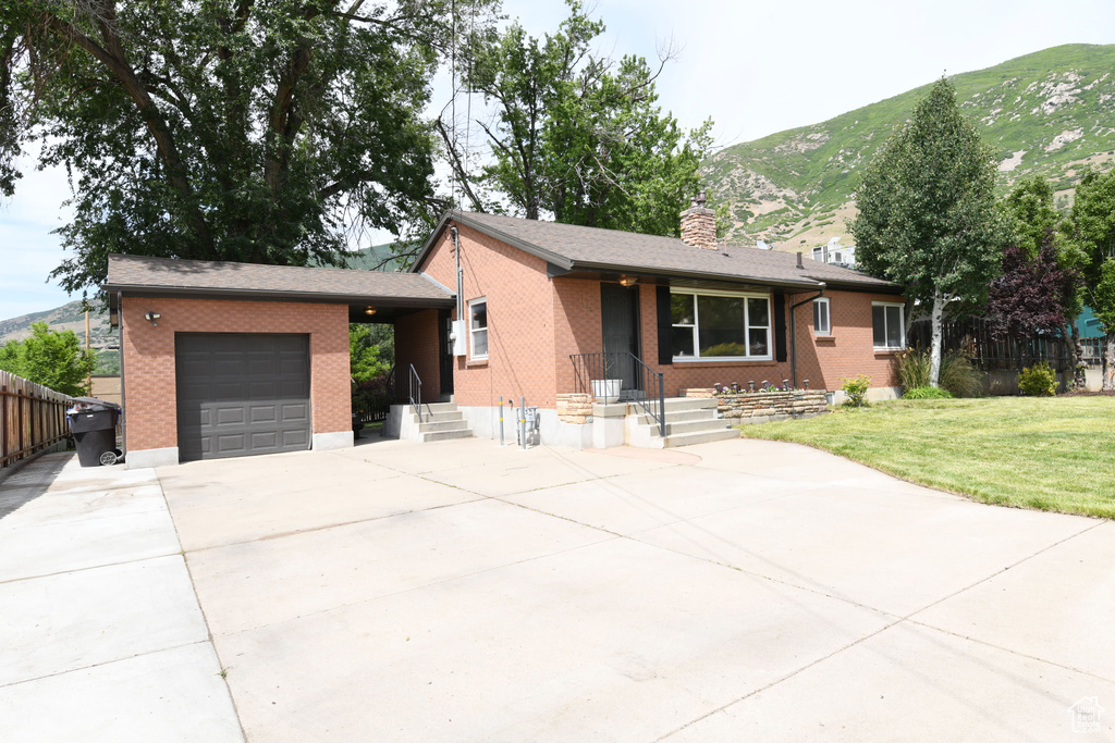 Ranch-style home featuring a garage, driveway, brick siding, a mountain view, and a chimney