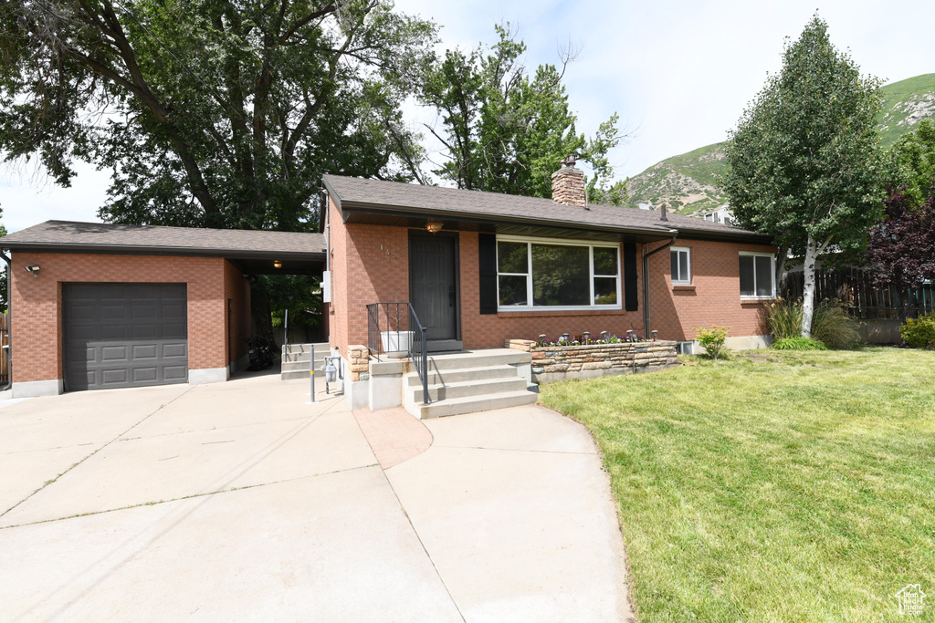 View of front of home featuring an attached garage, driveway, a chimney, and brick siding