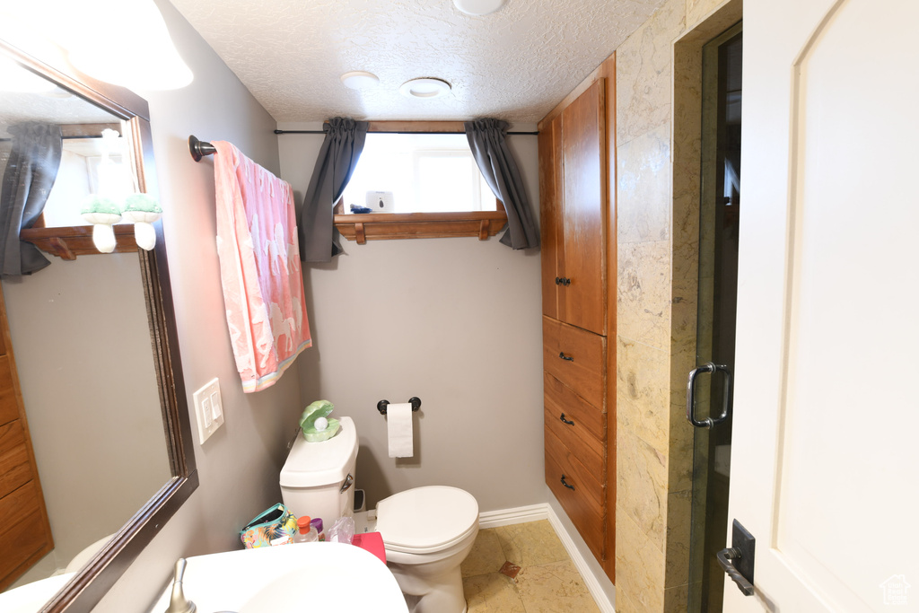 Bathroom featuring toilet, a textured ceiling, tile patterned flooring, and baseboards