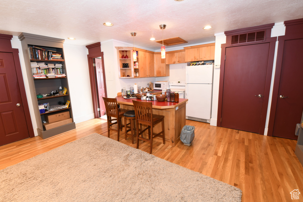 Kitchen with white appliances, open shelves, a peninsula, light wood-type flooring, and a kitchen bar