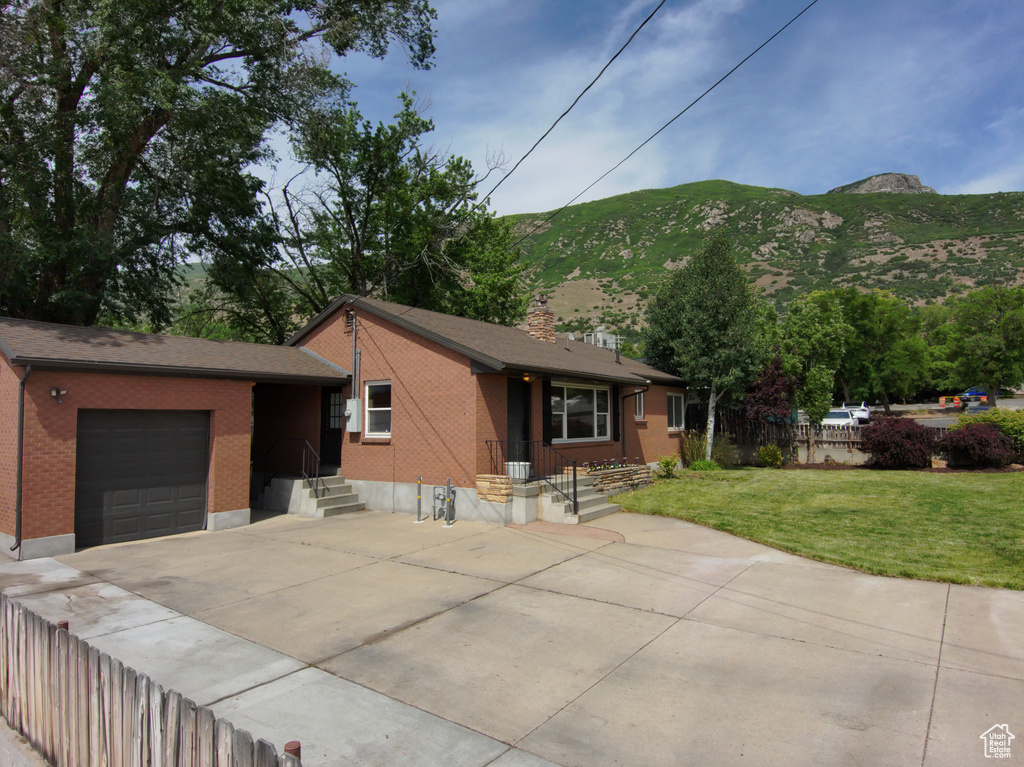 View of front of house with brick siding, concrete driveway, an attached garage, a mountain view, and a chimney