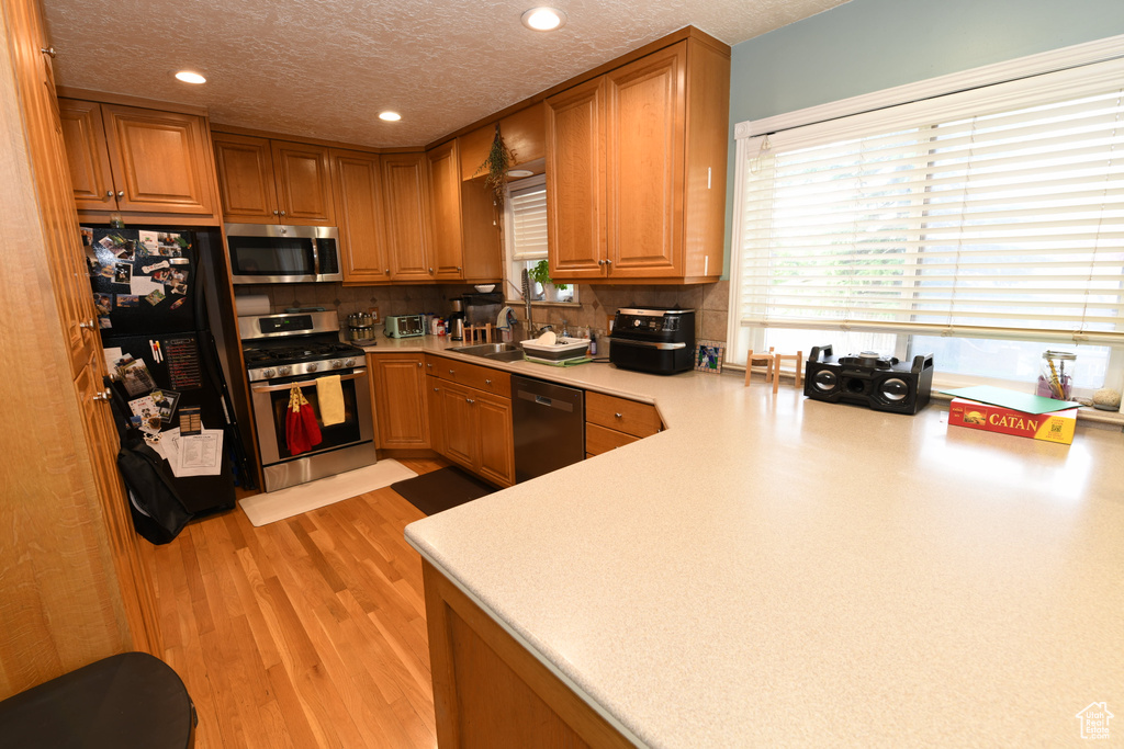 Kitchen with appliances with stainless steel finishes, a textured ceiling, recessed lighting, light countertops, and a sink