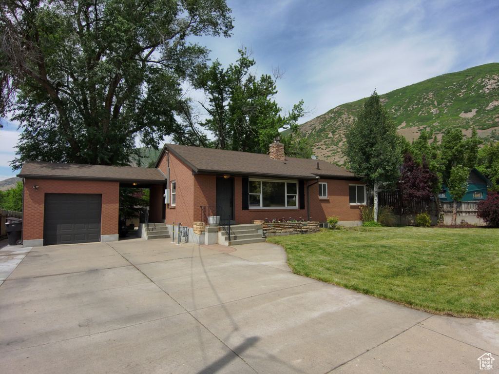 Single story home with a garage, brick siding, a mountain view, a front yard, and a chimney