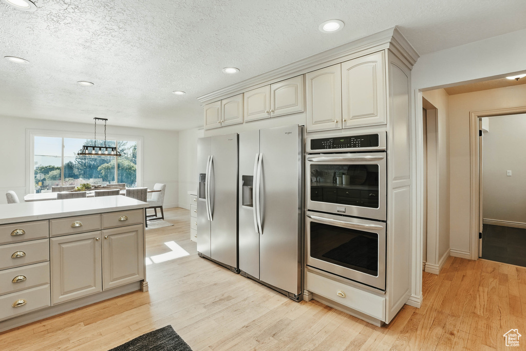 Kitchen with appliances with stainless steel finishes, light wood finished floors, recessed lighting, light countertops, and hanging light fixtures
