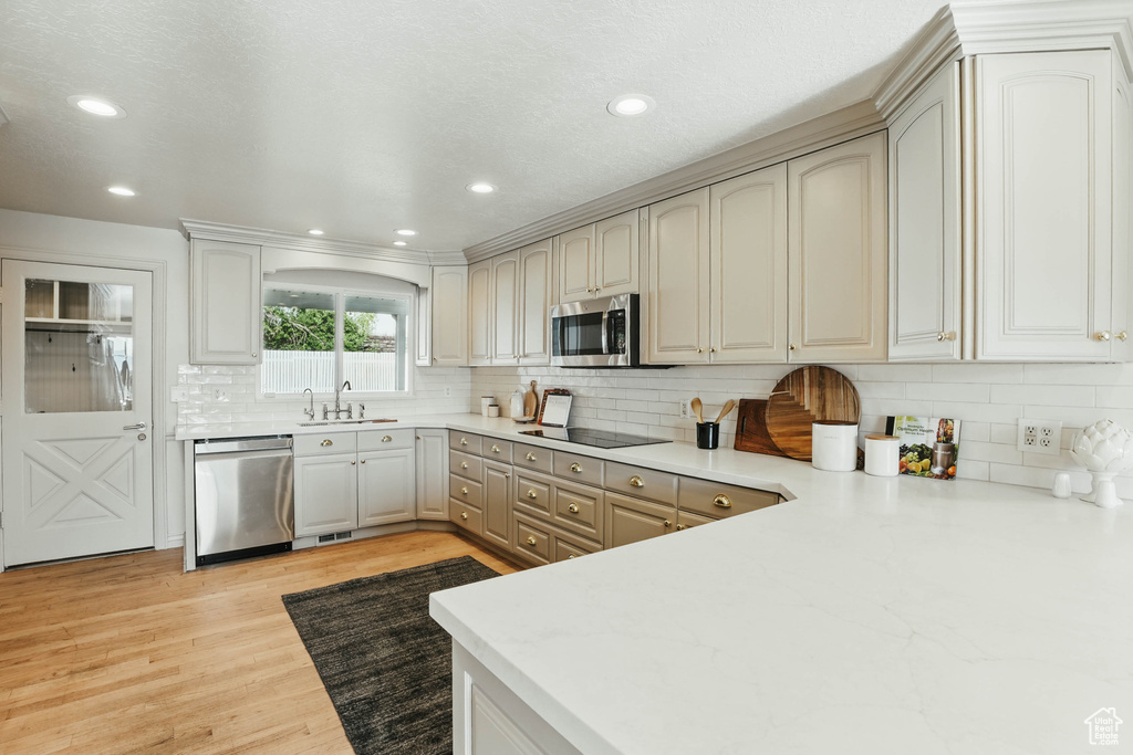 Kitchen featuring stainless steel appliances, a sink, light wood-type flooring, backsplash, and recessed lighting