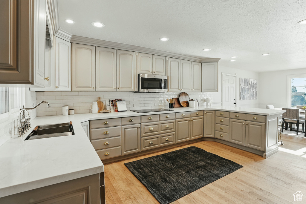 Kitchen with stainless steel microwave, a sink, a peninsula, light wood-type flooring, and black electric stovetop
