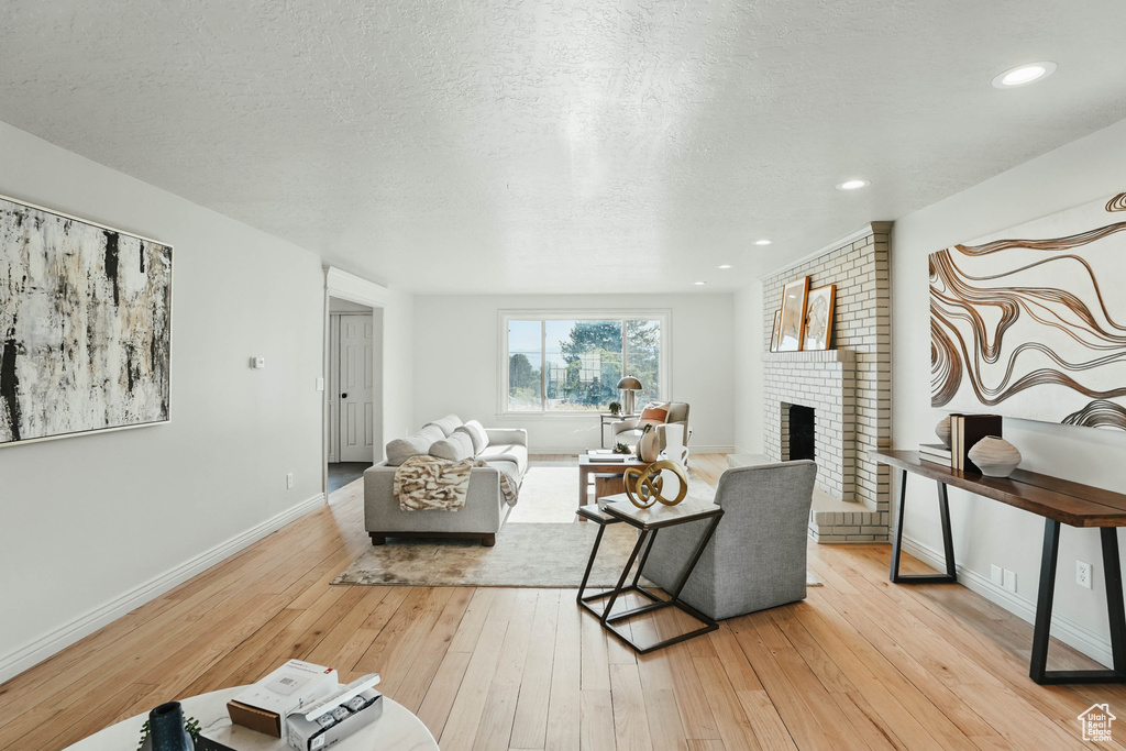Living room featuring light wood-style flooring, a brick fireplace, a textured ceiling, and baseboards