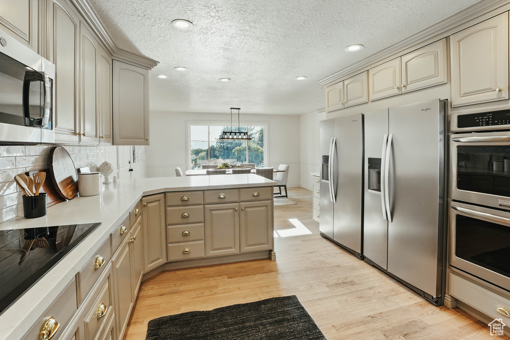 Kitchen with stainless steel appliances, a peninsula, cream cabinets, recessed lighting, and light wood finished floors