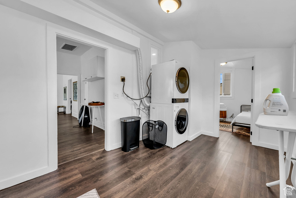 Washroom featuring stacked washer / drying machine, dark wood-style floors, and baseboards