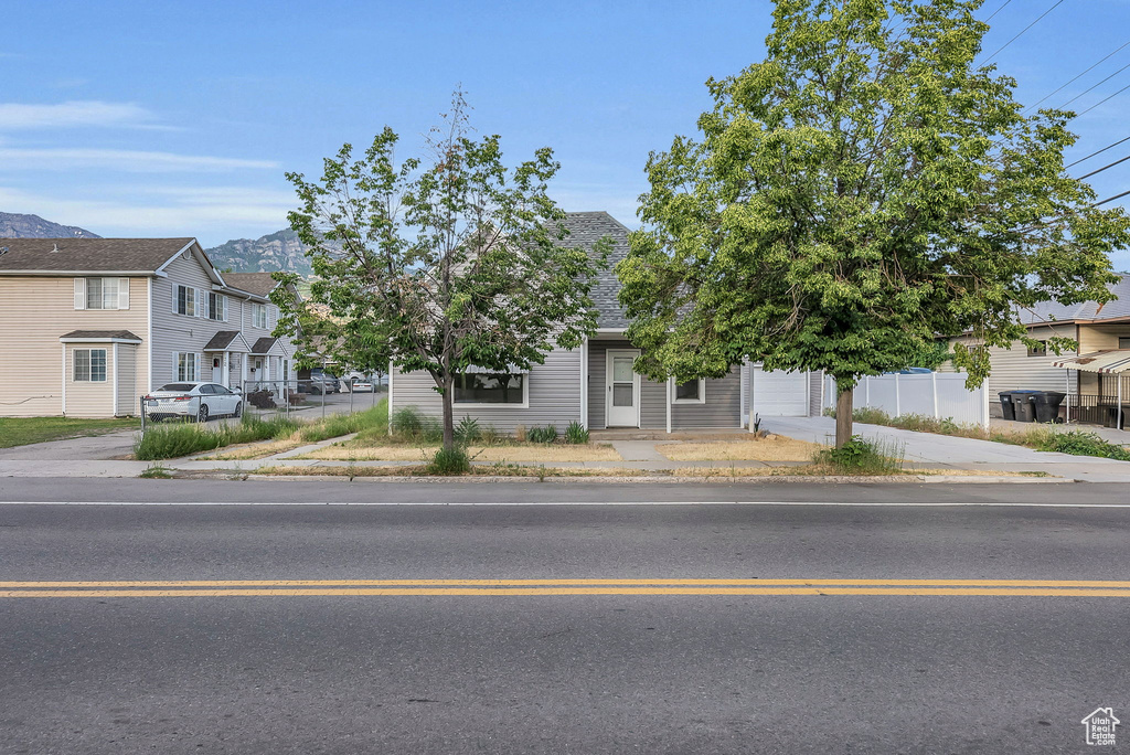 View of property hidden behind natural elements featuring concrete driveway, a mountain view, roof with shingles, and a residential view