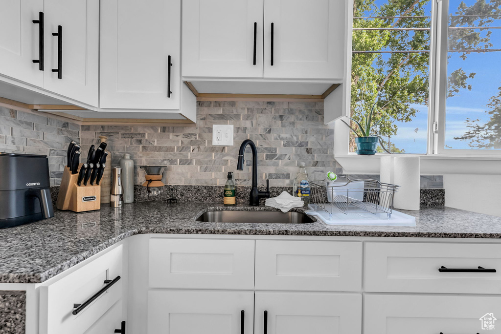 Kitchen featuring a sink, decorative backsplash, white cabinetry, and stone countertops