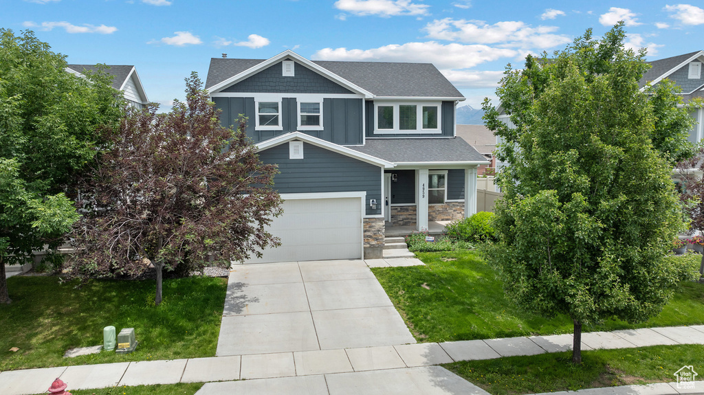 Craftsman-style home with concrete driveway, stone siding, a front lawn, roof with shingles, and a garage