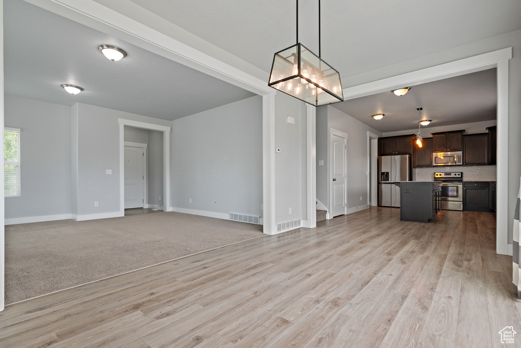 Unfurnished living room featuring light wood finished floors, baseboards, and a chandelier