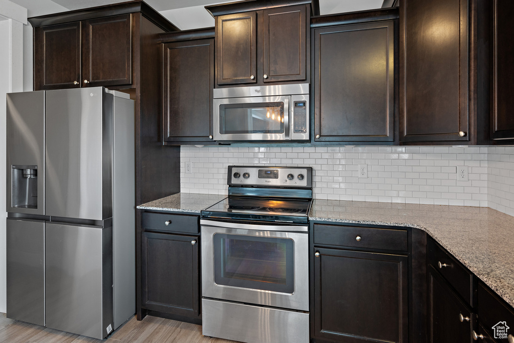 Kitchen featuring appliances with stainless steel finishes, dark brown cabinetry, light stone counters, and decorative backsplash