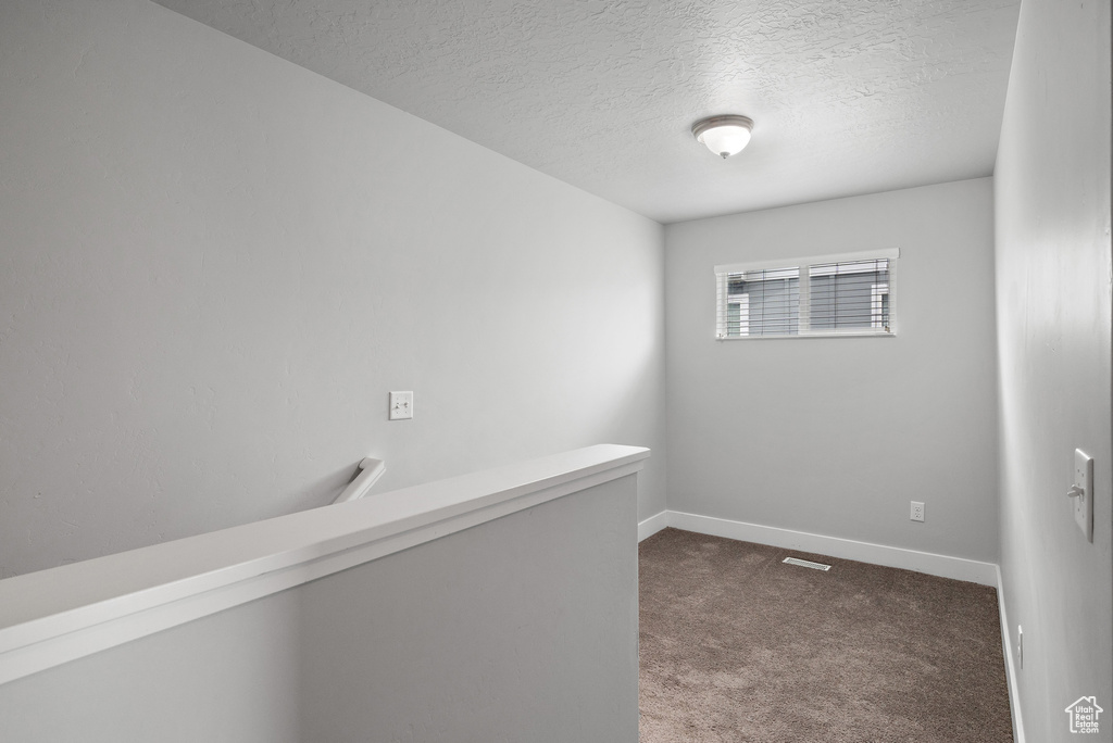 Carpeted empty room featuring a textured ceiling and baseboards