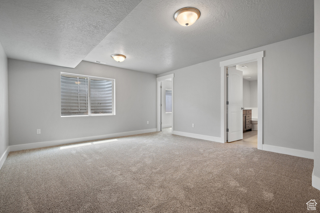 Unfurnished bedroom featuring a textured ceiling, light carpet, baseboards, and connected bathroom