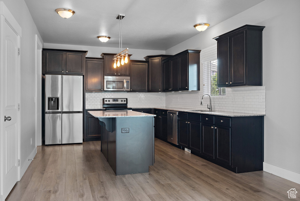 Kitchen featuring stainless steel appliances, a sink, wood finished floors, and light stone countertops