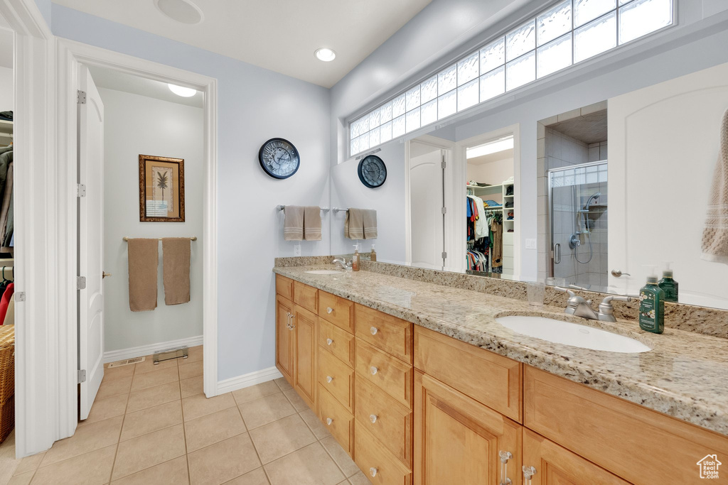 Bathroom with a walk in closet, double vanity, a shower stall, tile patterned flooring, and baseboards