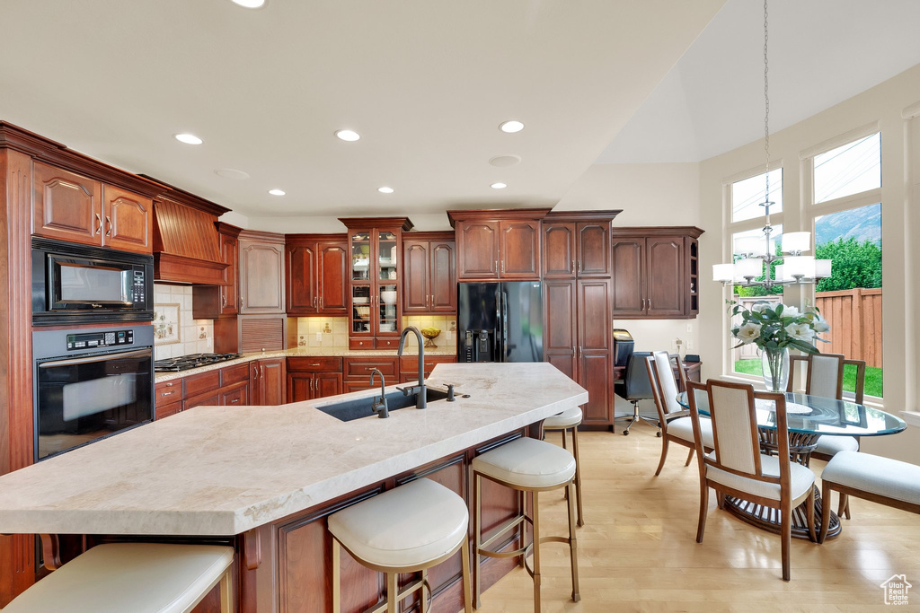 Kitchen with black appliances, a sink, a kitchen breakfast bar, recessed lighting, and light wood finished floors