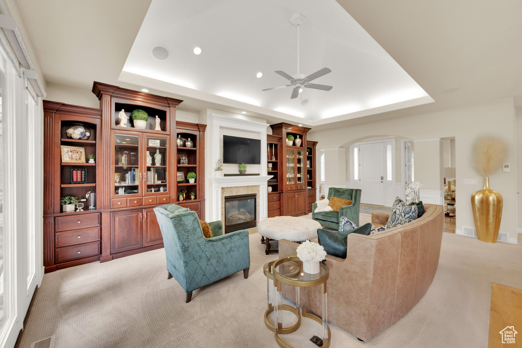 Living room featuring a raised ceiling, light carpet, ceiling fan, a glass covered fireplace, and recessed lighting
