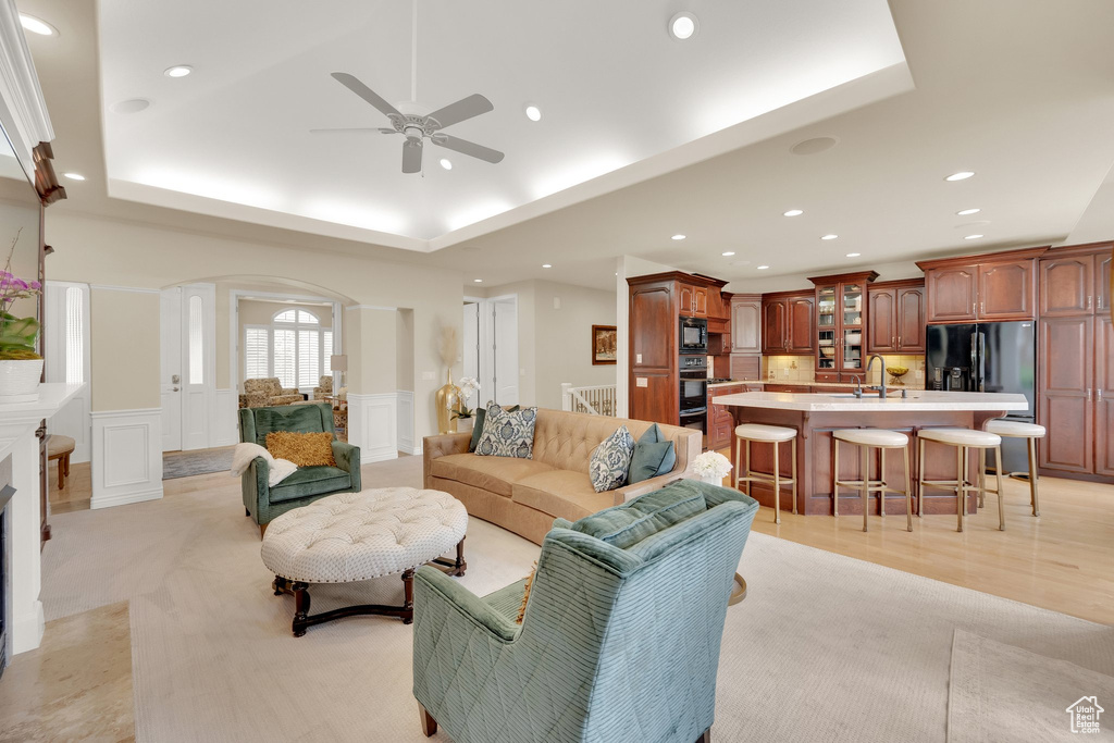 Living room with arched walkways, a raised ceiling, recessed lighting, a ceiling fan, and a decorative wall