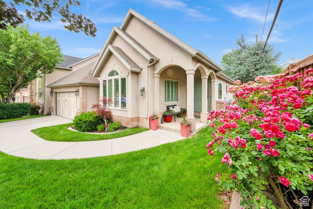 View of front of home with stucco siding, concrete driveway, a front yard, and an attached garage