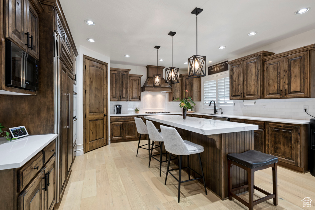 Kitchen with a sink, black microwave, a center island, light wood-style flooring, and a kitchen bar
