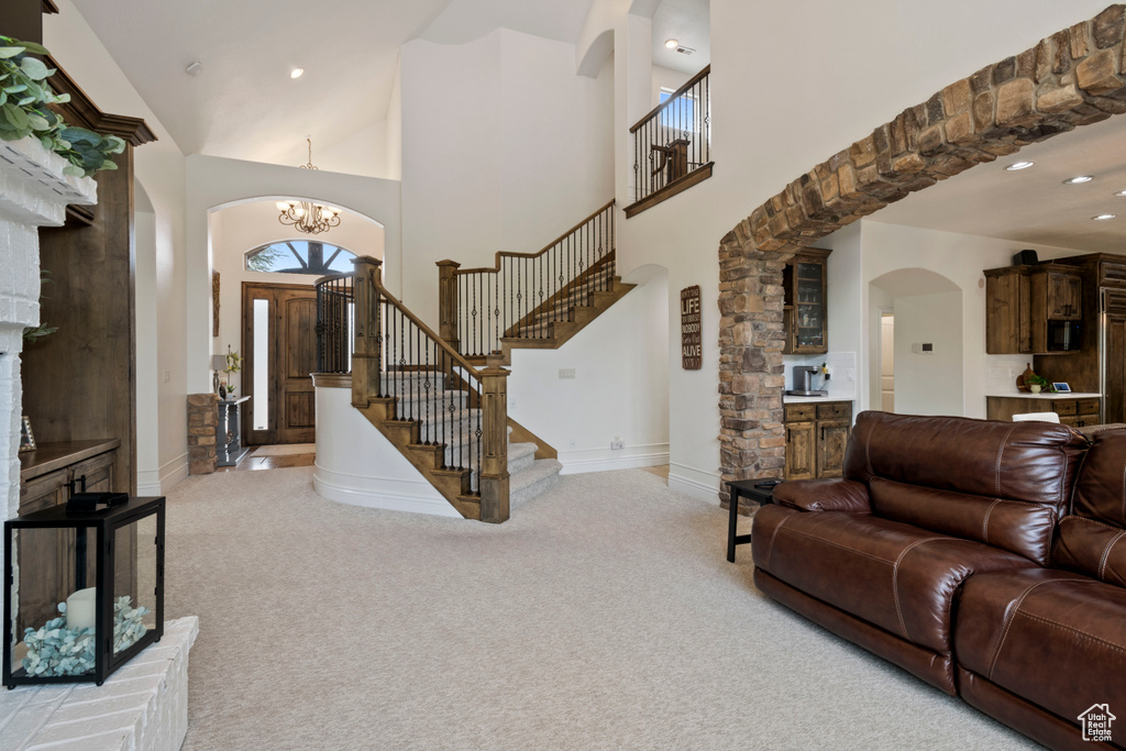 Living area with arched walkways, light colored carpet, stairway, a chandelier, and a high ceiling