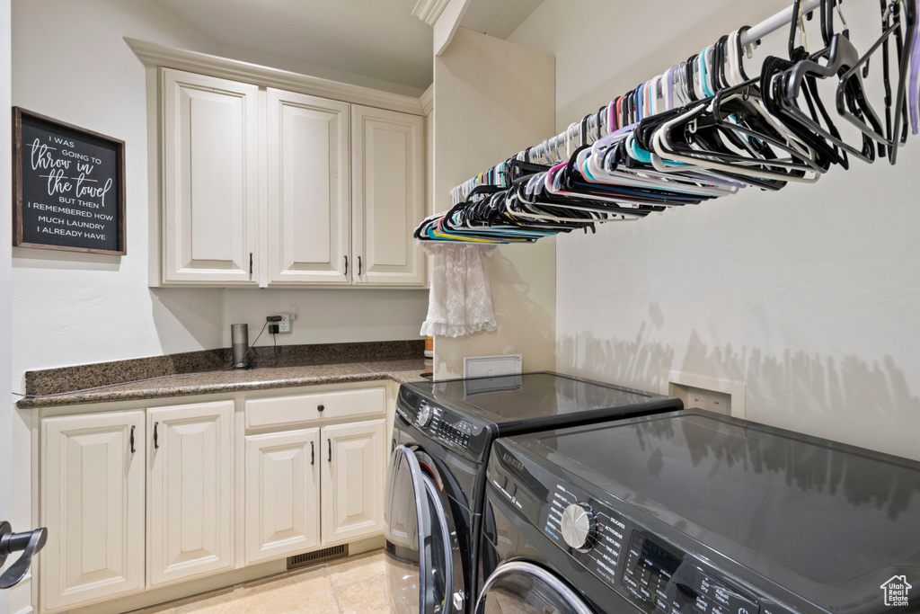Washroom featuring washer and dryer, cabinet space, and light tile patterned flooring