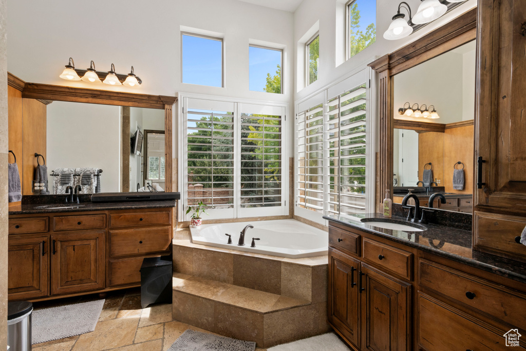 Full bath featuring stone tile floors, two vanities, a bath, and a high ceiling