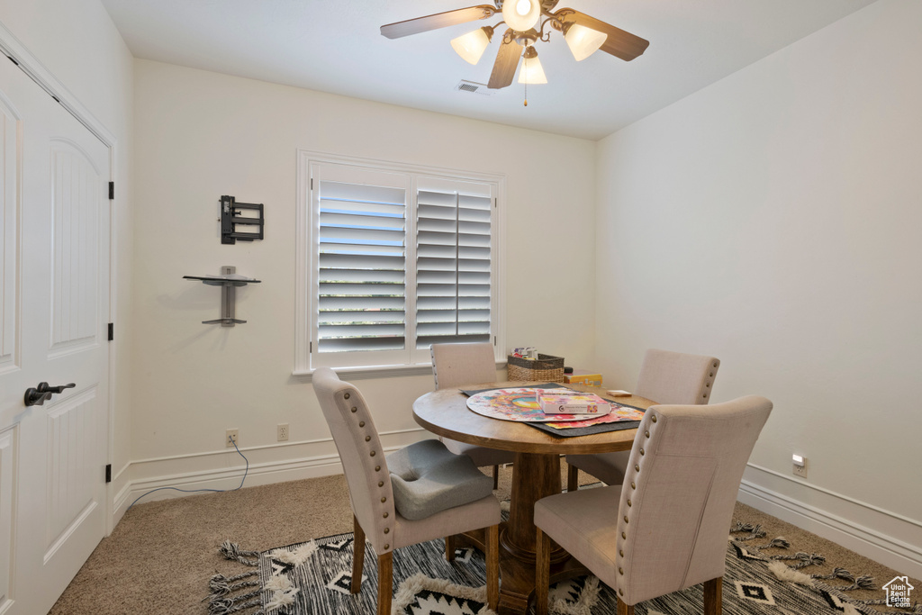 Carpeted dining area with ceiling fan and baseboards